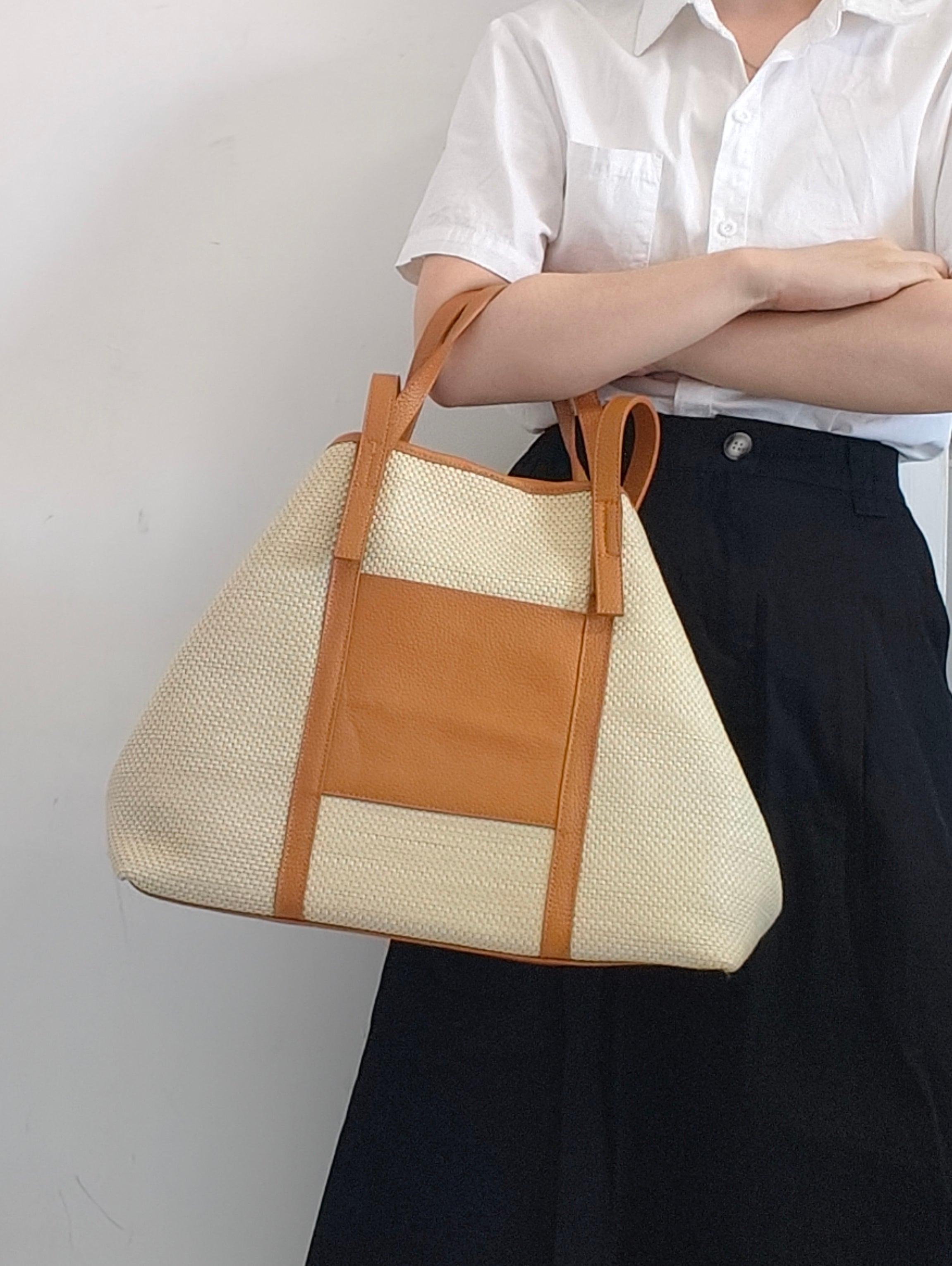 Marena-Borsa tote grande in rafia e vera pelle cuoio in un altro stile di forma trapezoidale portata al braccio da modella